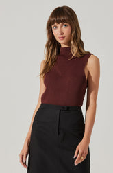 A woman is wearing a sleeveless, ribbed, high-neck top in a deep burgundy color with subtle vertical stripes and seam detailing on the front. She pairs it with a high-waisted black skirt that has a front button and two horizontal pocket flaps.